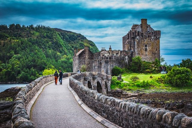 A stone castle reached by a footbridge, with people walking across