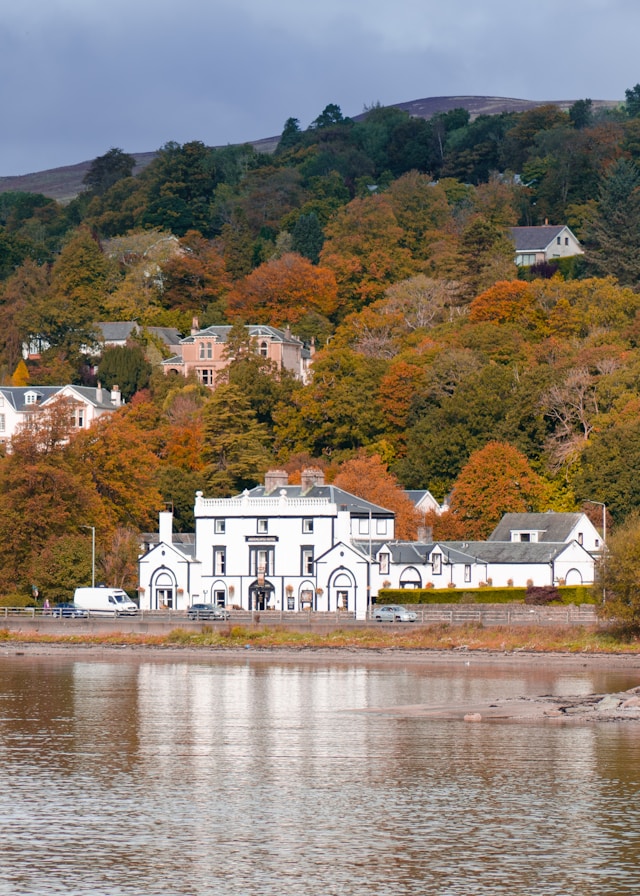 A peaceful house among autumn trees by the water, representing Rowan Cabin's cosy, burn-side setting