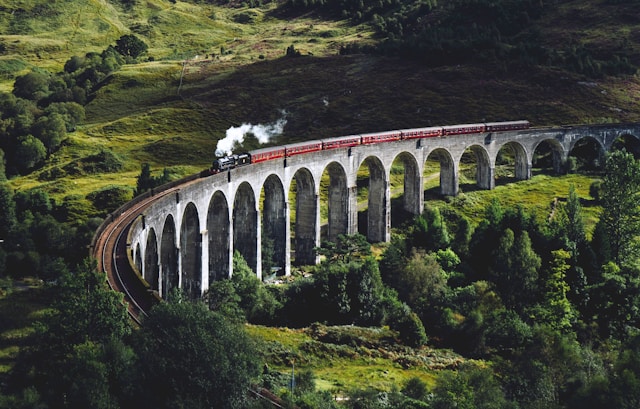 A steam train crossing a stone viaduct through green summer hills