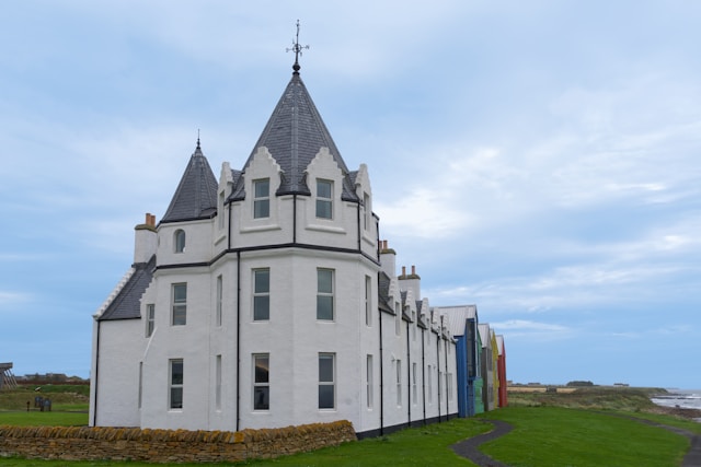 A white turreted highland building on the coast under a pale sky