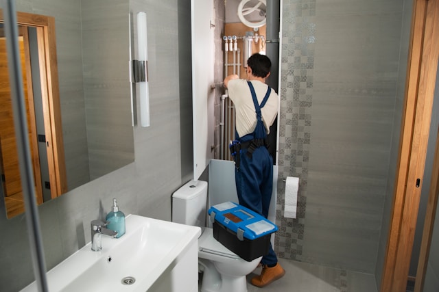 A plumber fitting pipework behind a toilet cistern in a modern bathroom