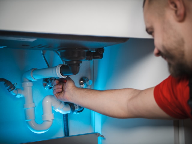 A plumber working on pipework under a bathroom sink, lit in blue light