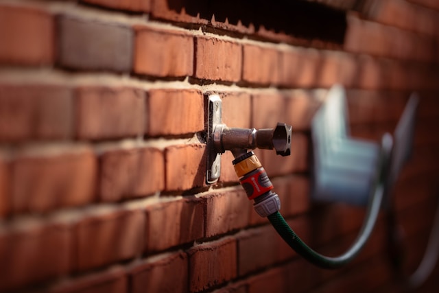 An outdoor tap fitted to a brick wall with a hose attached