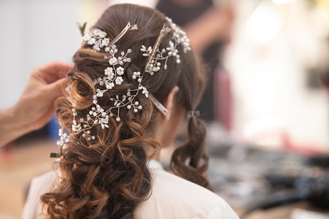 An intricate bridal updo being finished with a pearl hair vine