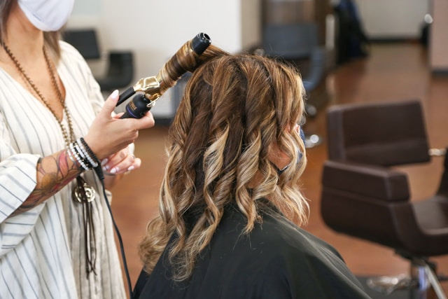 A stylist curling a client's freshly coloured, highlighted hair